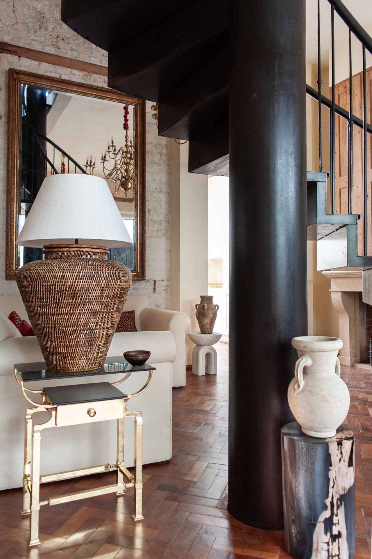 rattan lamp on brass and glass side table by cream sofa and petrified tree stump with terracotta amphora
