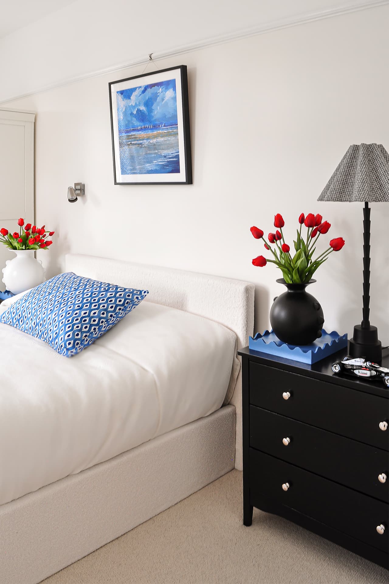 cream bedroom with cream bed, black bedside drawers, blue cushion on bed and blue curtains