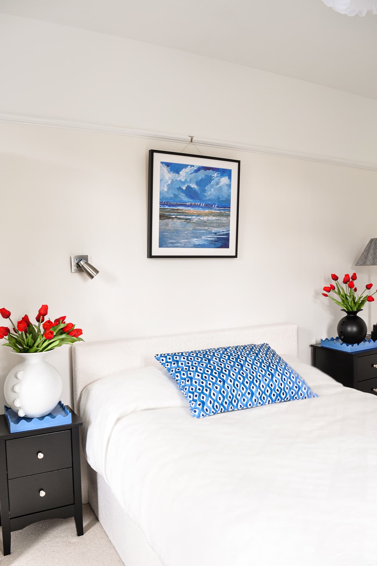 cream bedroom with cream bed, black bedside drawers, blue cushion on bed and blue curtains