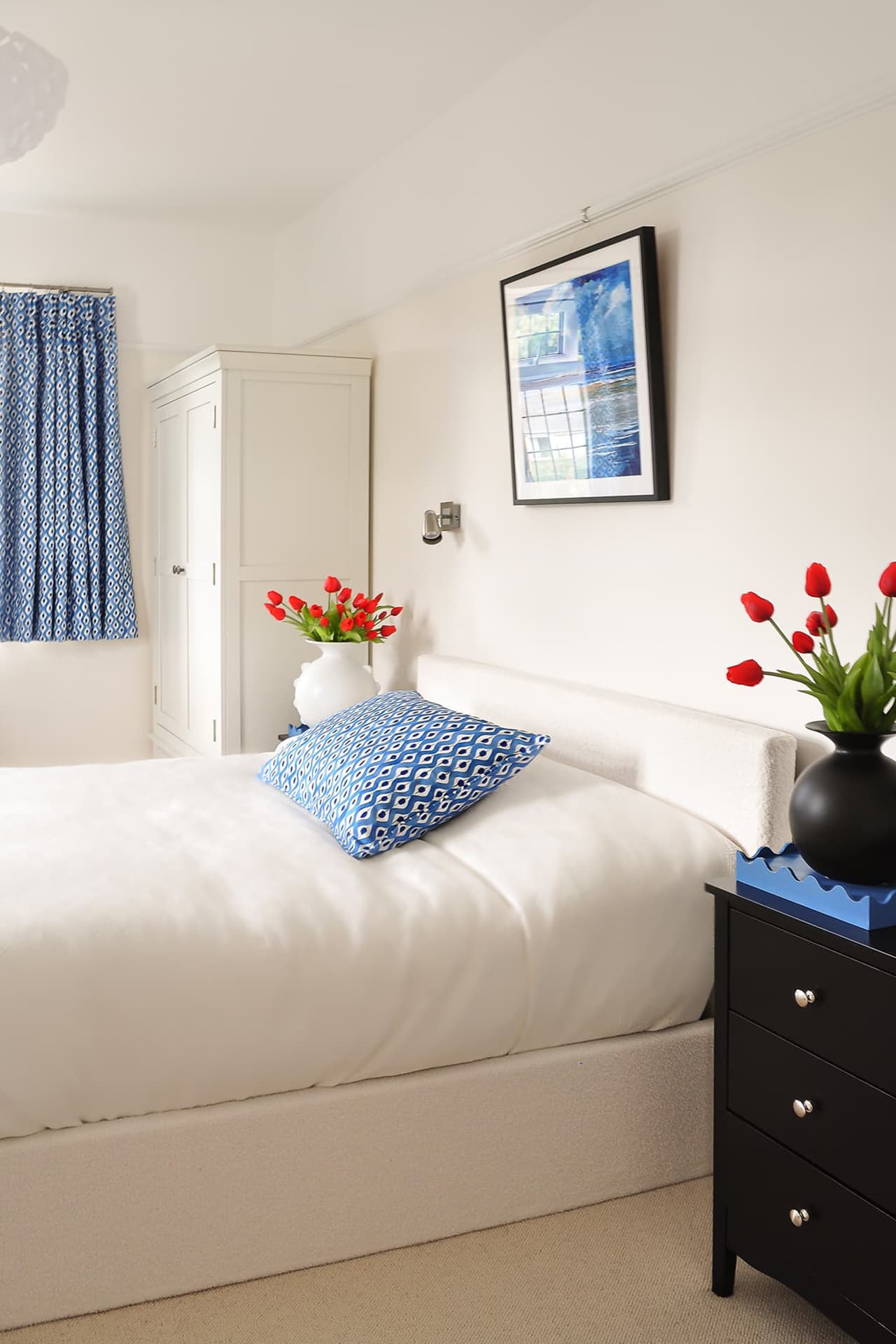 cream bedroom with cream bed, black bedside drawers, blue cushion on bed and blue curtains